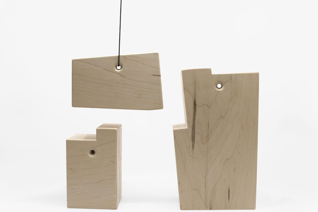 Three pale wooden blocks with stepped profiles on a white ground, the upper one hanging from a cord