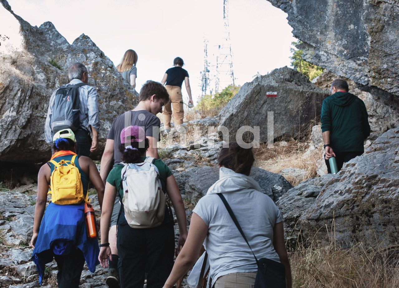 A group with backpacks climbing a rocky path between limestone outcrops toward a ridge